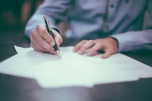 Männlicher Student beim Unterschreiben von Unterlagen an einem Schreibtisch